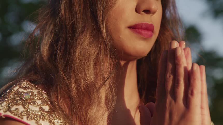 Close up of a woman with hands clasped in prayer outdoors at sunset