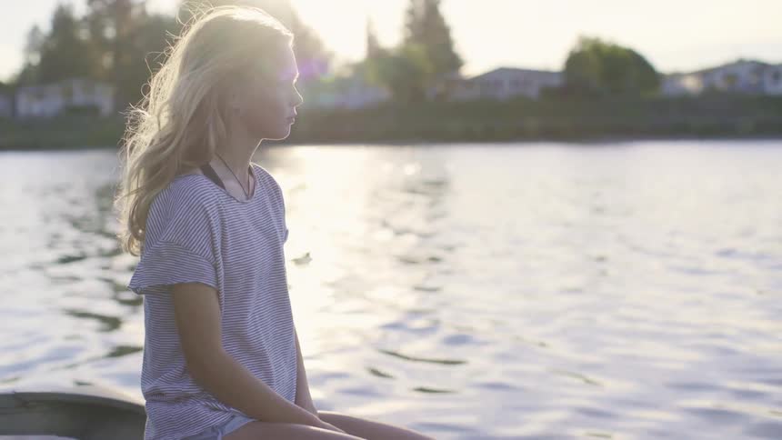 A blonde woman sits on the edge of a boat looking at the water