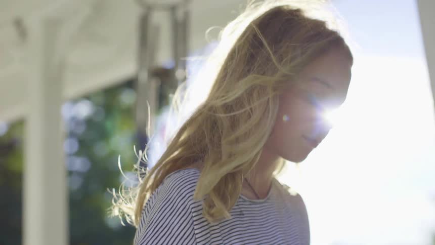 Blonde girl stands under porch on windy sunny day