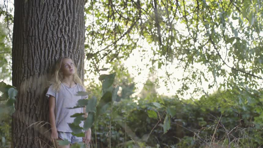 Girl with long hair leaning against a large tree trunk in the woods