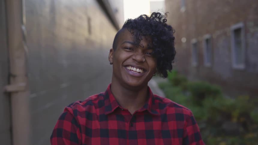 Man standing in an alley at daytime smiling and laughing at the camera