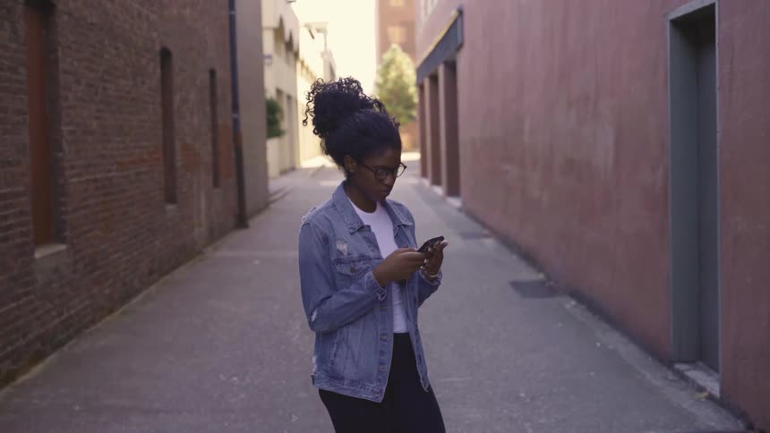 A teenage girl stands in an alley and texts
