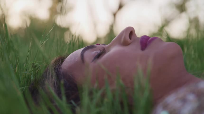 A woman is lying in grass with her eyes closed
