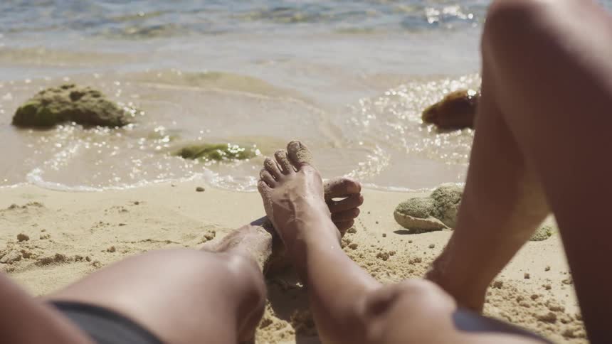 A male and female lay on the beach while relaxing on a sunny day