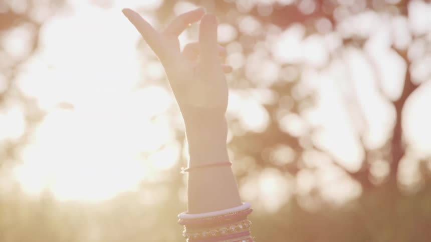 A woman stands with her hand in the air as the sun shines down