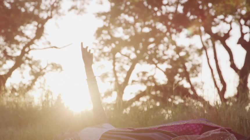 A woman lying in the grass with her arm extended towards the sky