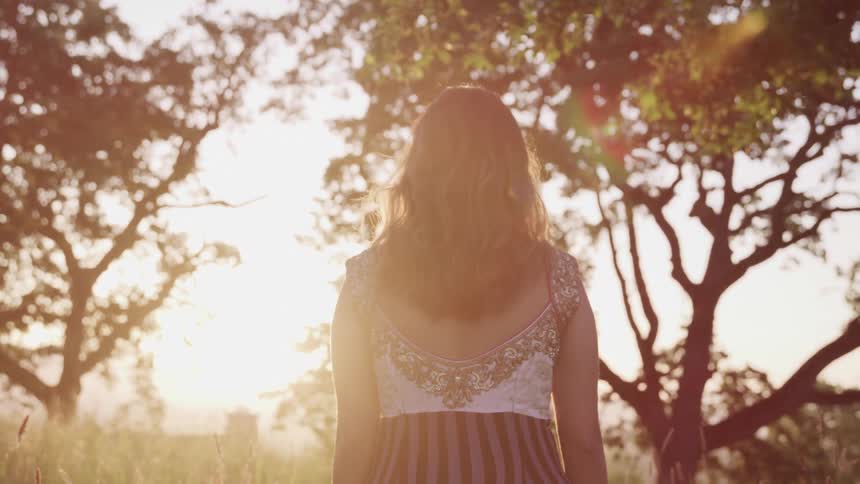A young woman walks towards a tree in the distance