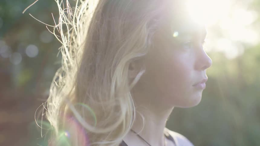 A young girl stands outside as the wind blows her hair and sunlight shines upon her
