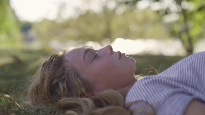 Woman resting over the grass under the tree shadows near a lake outdoors