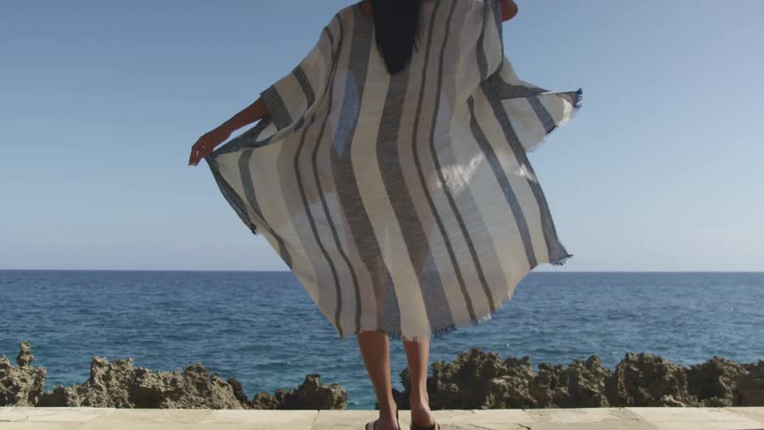 Wind blowing over the thin robe a woman in swimsuit wears in front of the ocean