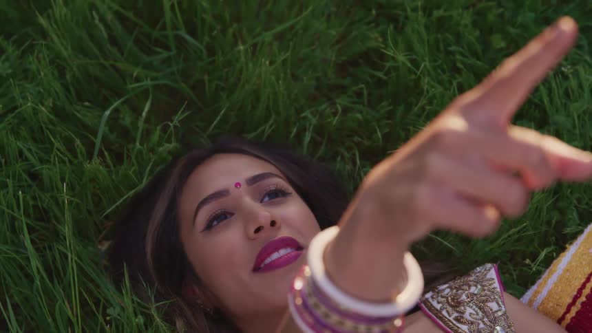 Young hindi woman with a bindi on her forehead lays on the grass pointing at the sky