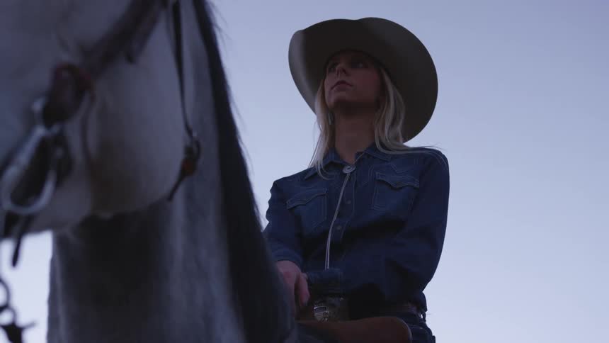 Woman wearing a cowboy hat sitting on a horse at evening
