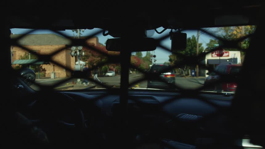 A police car pulls up behind a minivan at a stop light in a city neighborhood