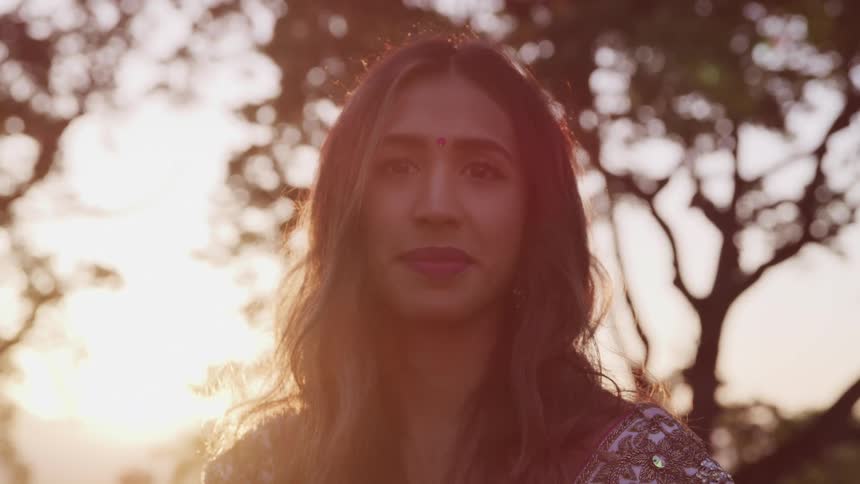 A young indian woman in traditional clothing stares into the camera while standing outdoors at sunset