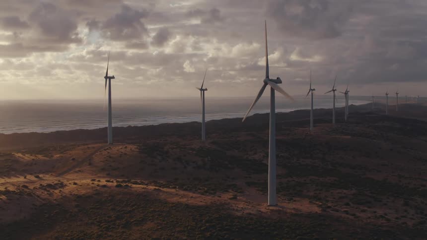 Wind turbines spinning on a wind farm in the field near the ocean at sunset