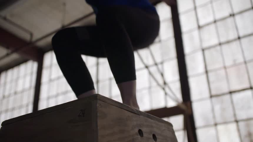 Woman in a gym jumping on and off of a wooden box