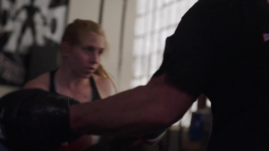 A female boxer spars with a trainer in a gym