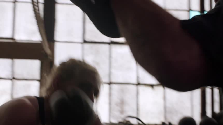A female boxer practices punches in a gym with large windows