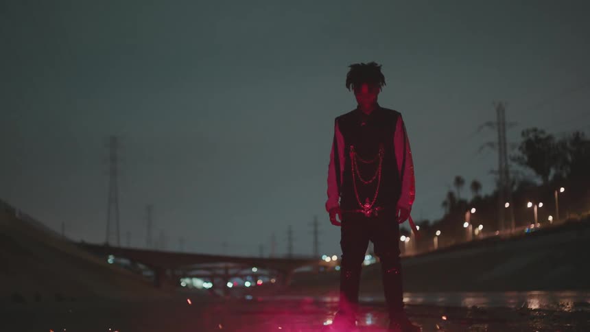 A teenage male stands outside at night in front of a burning fire