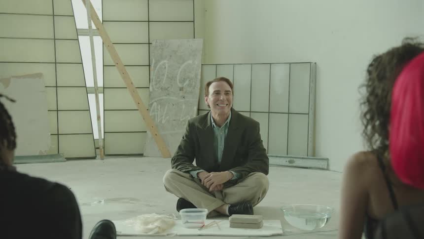 Man enters a room and sits down on the floor smiling in front of a crowd of young people