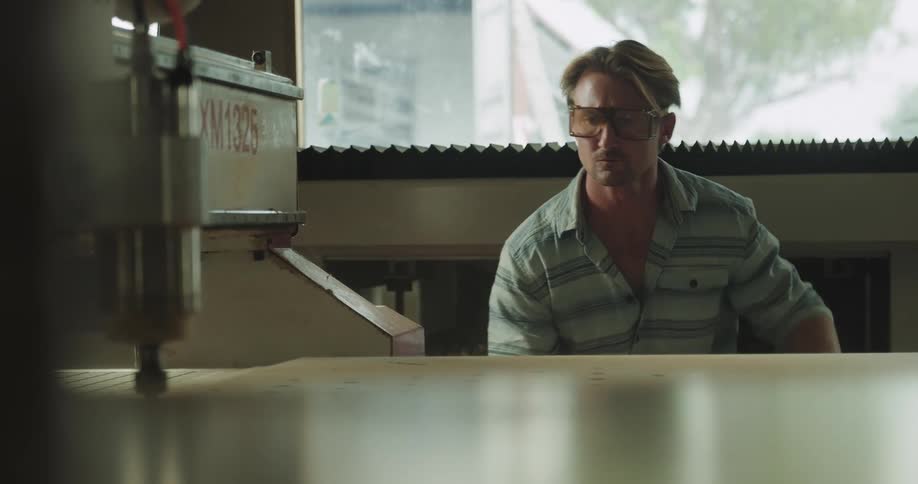 Man wearing protective glasses supervises a machine drilling on a surface inside a warehouse