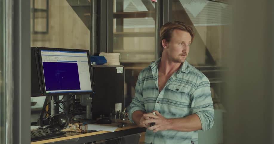 A man stands in front of a computer with his hand on the mouse and turns around