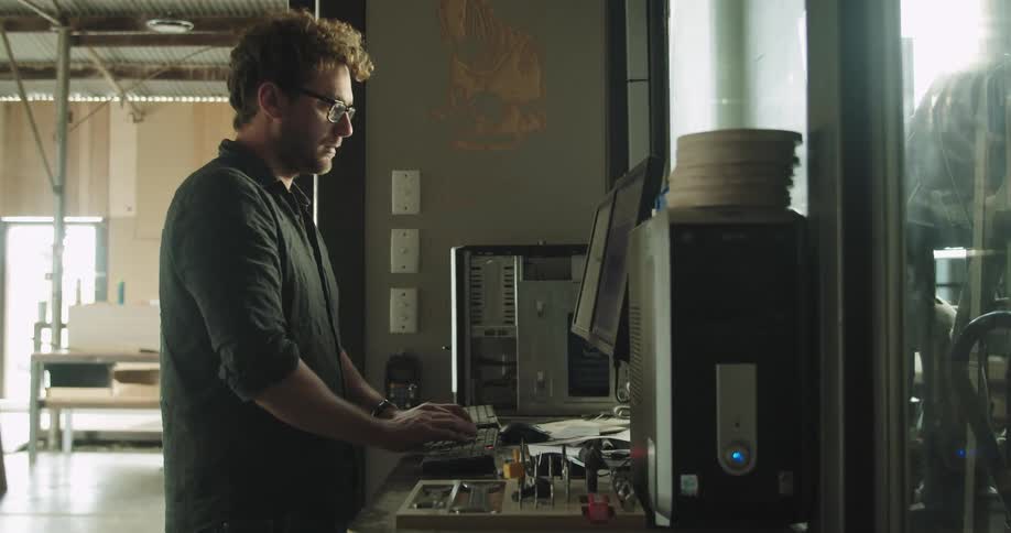 A man types on a computer at a standing desk inside a building under construction