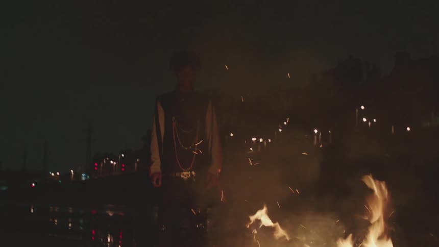 A young male stands next to a pile of debris that is completely engulfed in flames