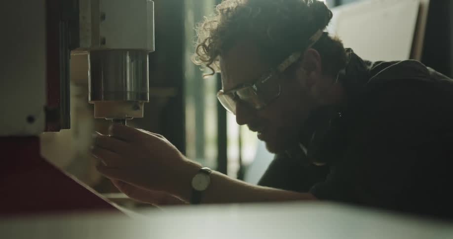 Man crouches to change a piece on a machine in a factory inside a warehouse