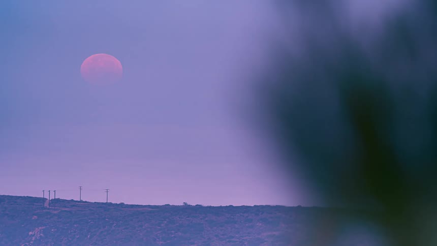 Time lapse of a big red moon setting over the horizon at sunrise