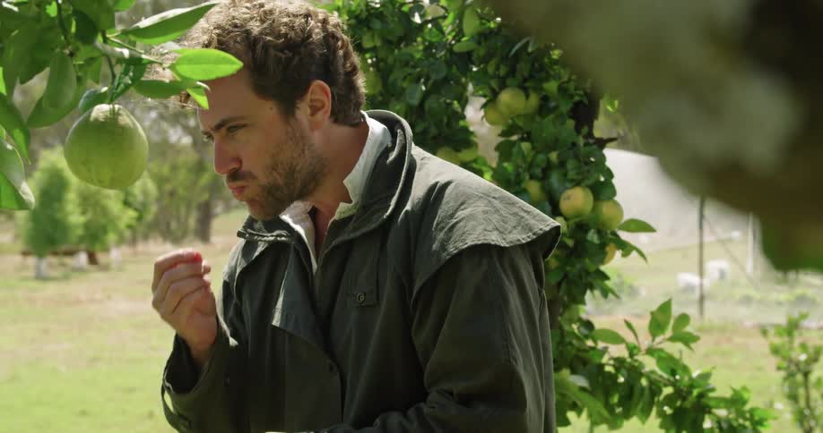 A man stands in a vineyard and eats a piece of fresh fruit
