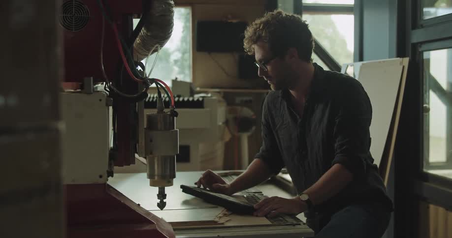 Man guides machine moving across table via keyboard in workshop