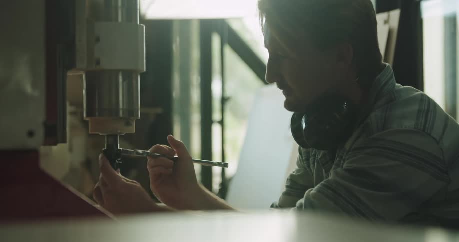 Man using tools to change the tip of a drill on a machine in a workshop