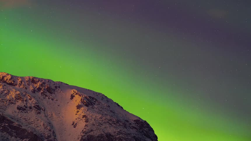 A timelapse of clouds and stars moving over a snow covered mountain