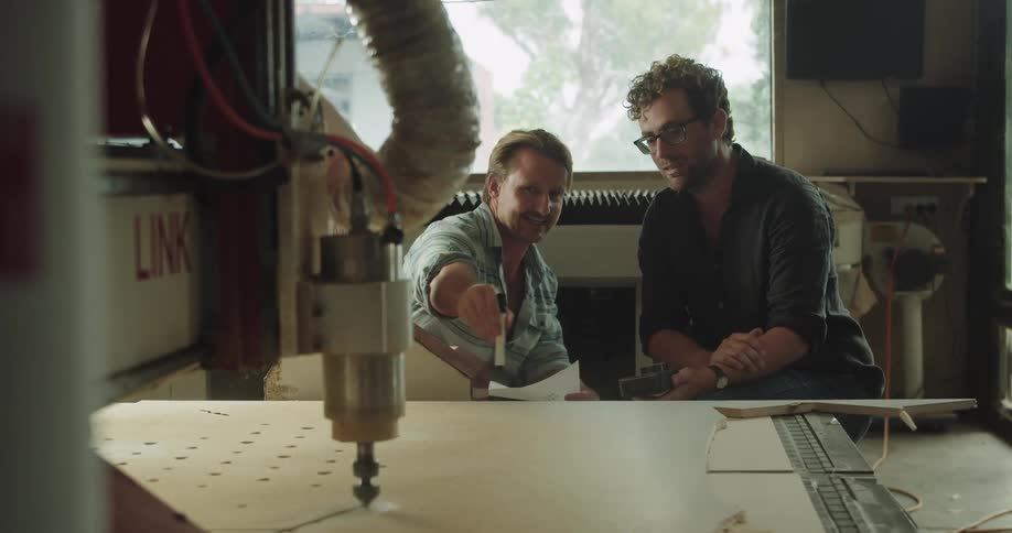 Two men sit beside each other in a workshop talking about the project in front of them