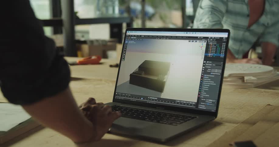 One man looks at a laptop while another man gathers supplies in a factory