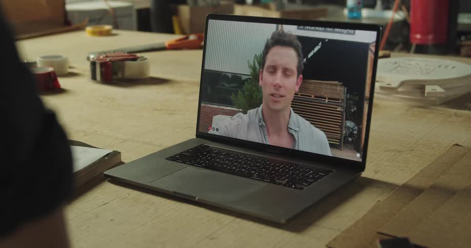 A person in a workshop talks with a man through video chat on a laptop