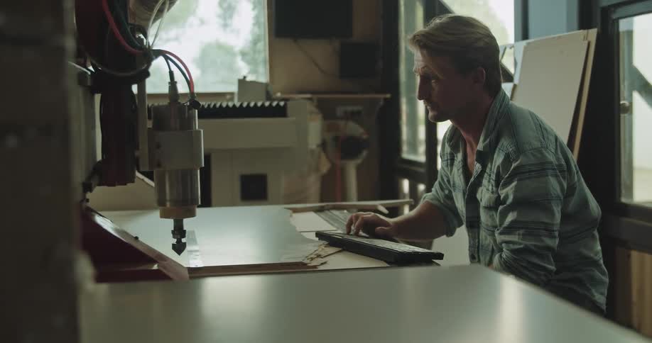 A man sits in front of a keyboard and a machine and adjusts items beneath it