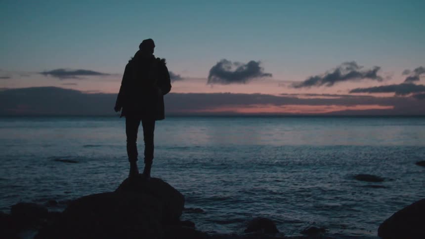 Someone standing on a boulder on a shoreline as the sun sets