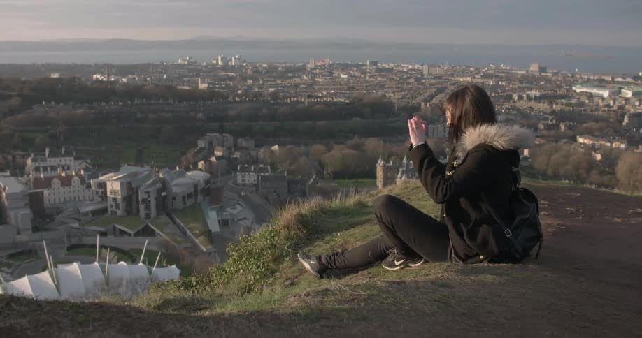 A woman is taking photographs as she sits on a hill