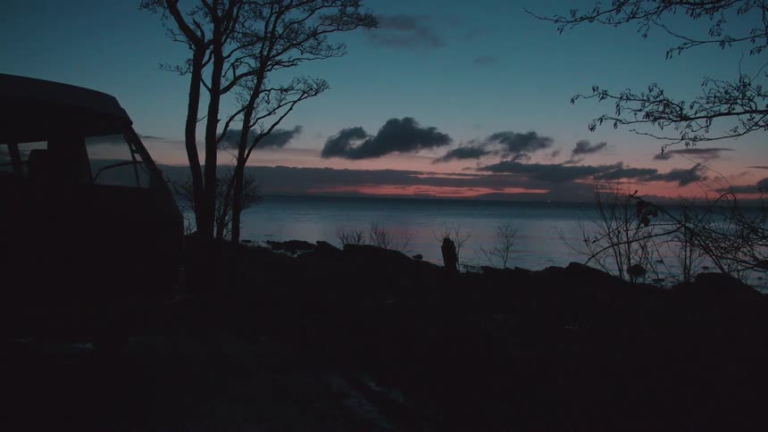 A van is parked on the bank overlooking the water at sunset