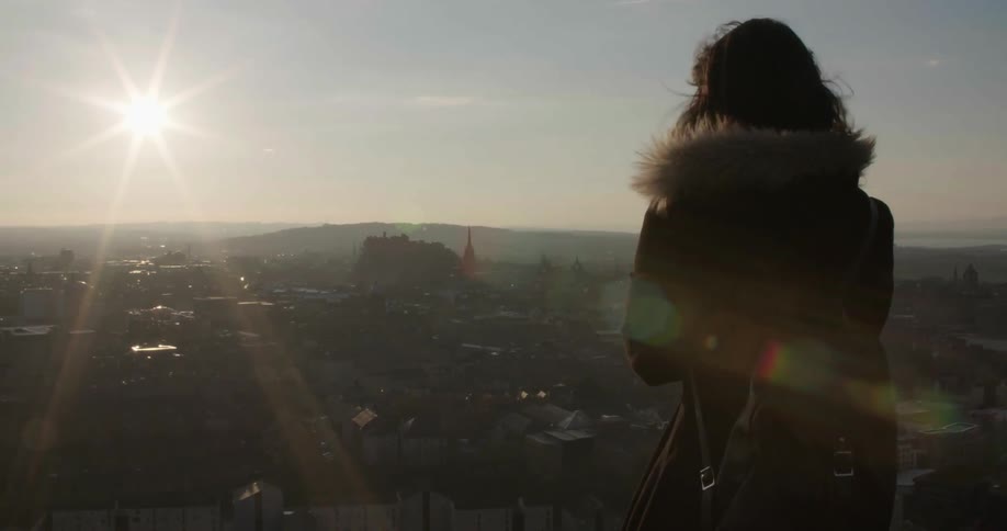 A woman is standing above a city on a windy day
