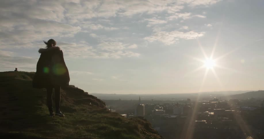 A woman walks to the top of a hill overlooking the city