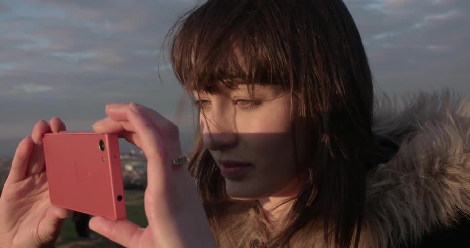 A woman is taking a photo with her phone on a windy day