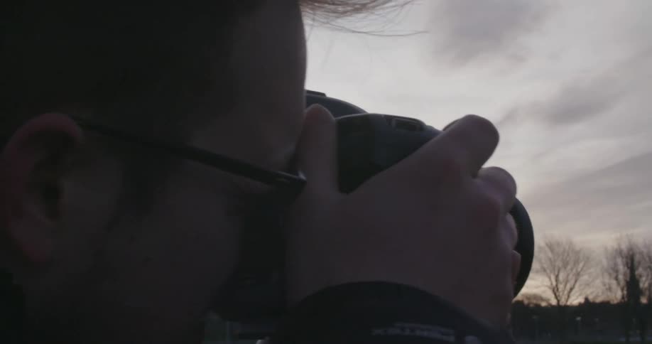 A man raises a camera and takes a picture at sunset