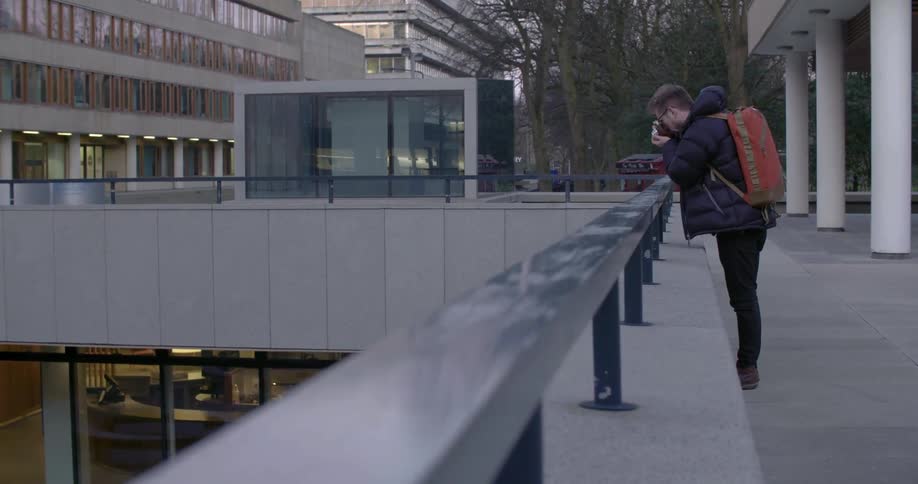 A man leans over a railing and takes a photograph on a winter day