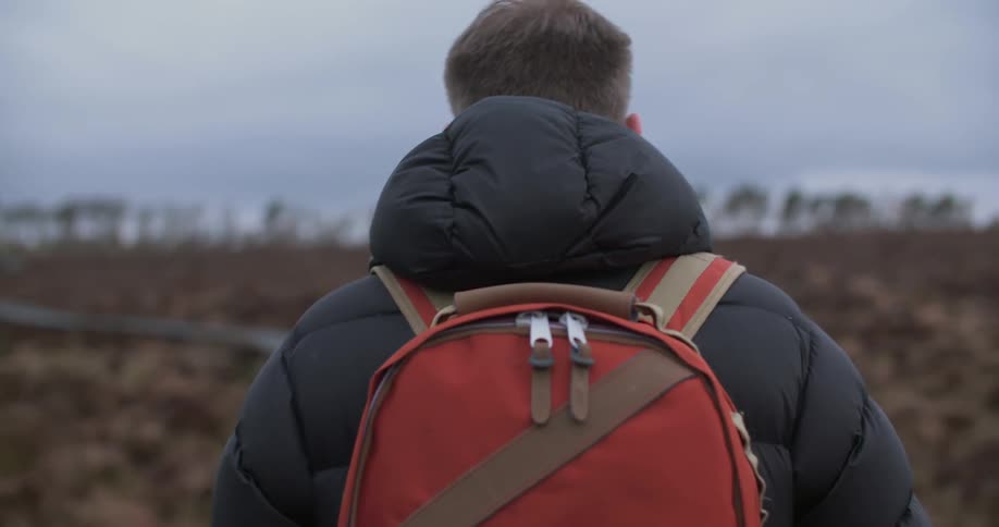 A man with a backpack walks down a path on a gloomy day