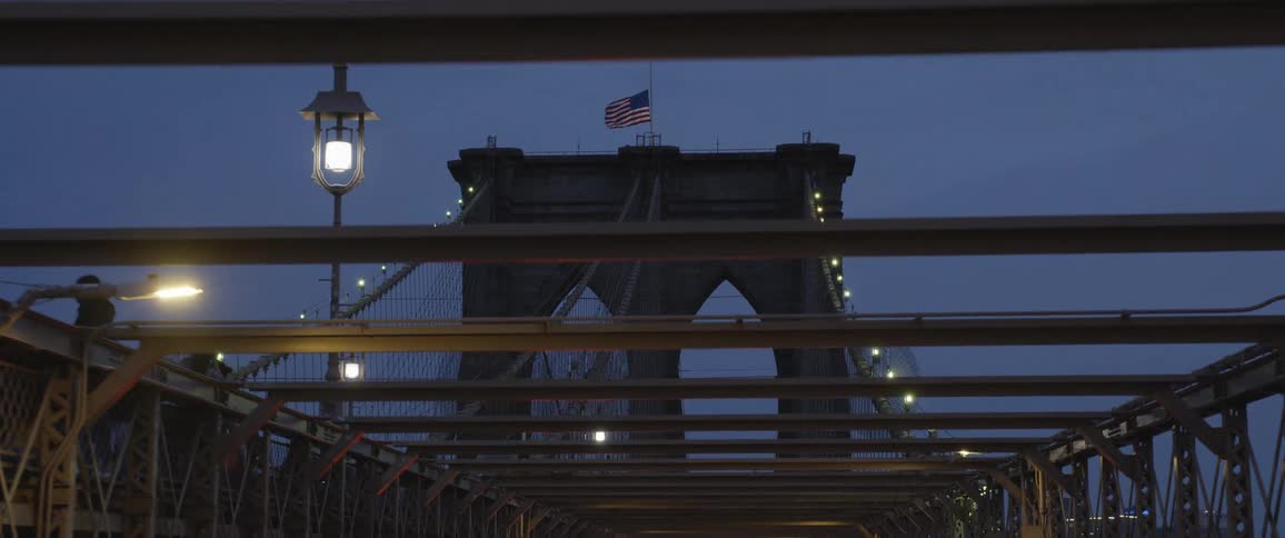 An american flag atop the tower of a bridge waves in the wind at night