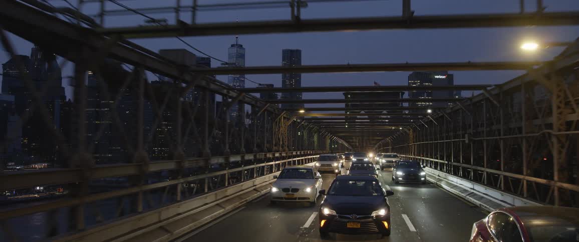 Dense traffic travels on a bridge across a waterway in a metropolis at night
