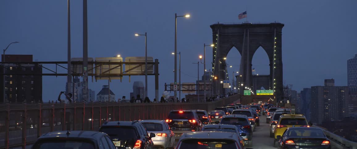 People walk across a bridge as cars drive across it